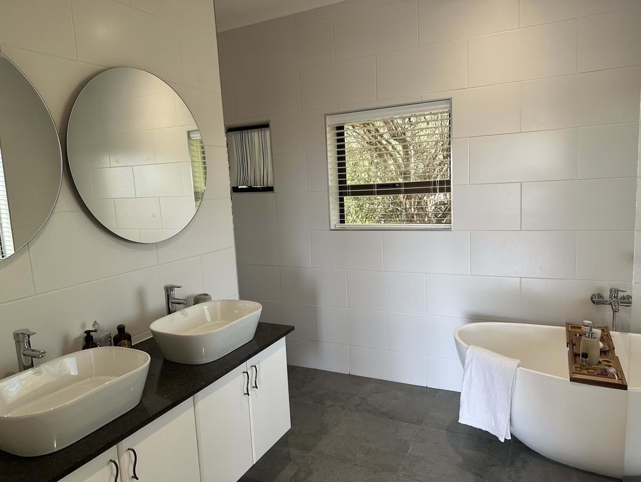 A modern bathroom with twin basins under round mirrors and a freestanding bath