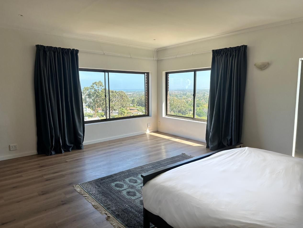 A spacious bedroom with dark curtains and windows on two sides looking towards the bay